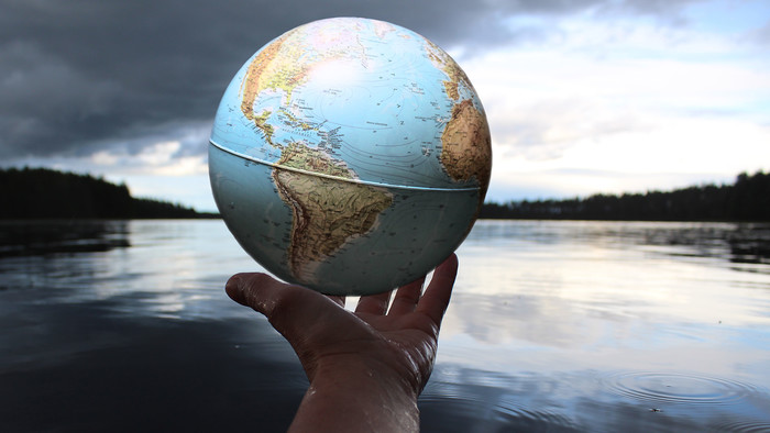 Eine Hand hält einen Globus vor einem See