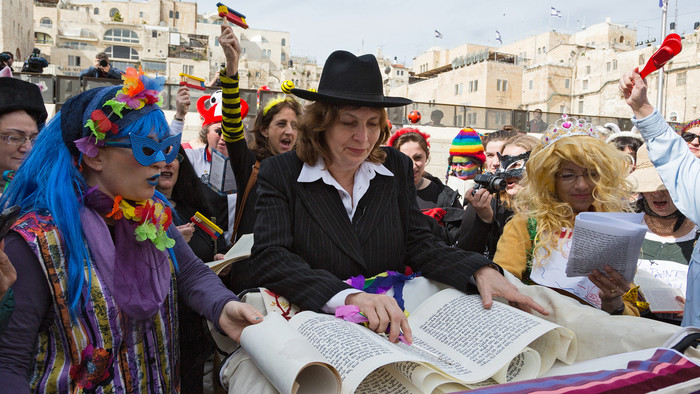 Frau liest laut aus Buch Esther, verkleidete Frauen stehen um sie herum