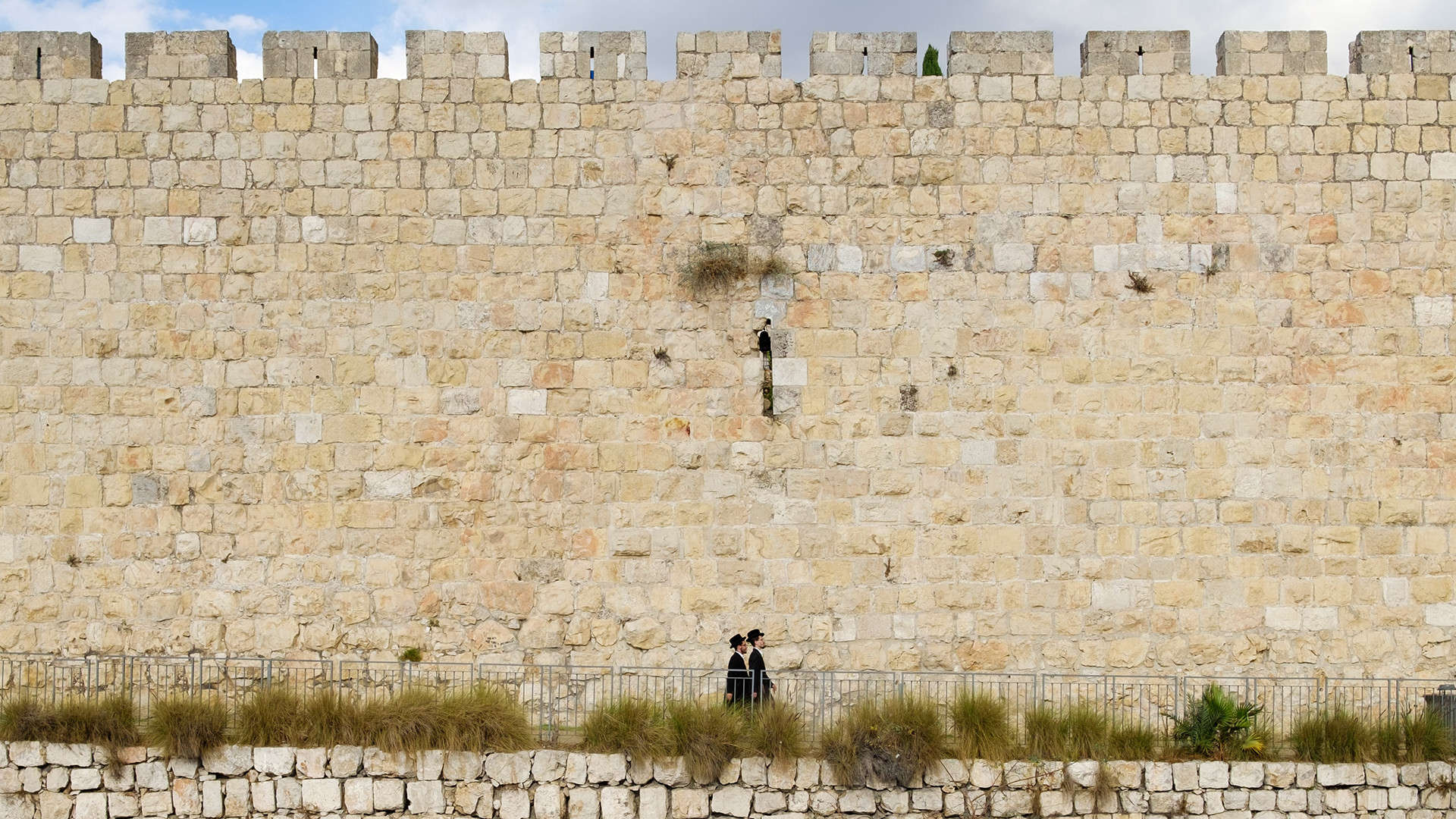 Zwei jüdische Männer laufen vor einer hohen Mauer
