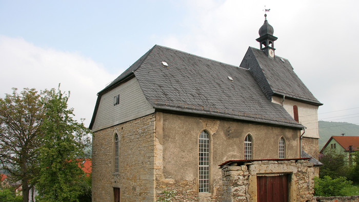 Schlichte Kirche aus hellem Stein mit dunklem Dach und schmalen, hohen Kirchenfenstern