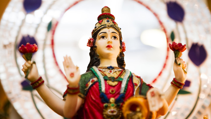 Statue der Hindu-Göttin Lakshmi mit roten Lotusblüten in beiden Händen.