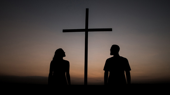 Mann und Frau stehen vor Kreuz bei Sonnenuntergang