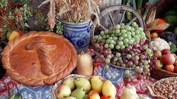 Obst, Gemüse, Getreideähren und ein mit einem Kreuz verziertes Gebäck auf einem Tisch angerichtet.