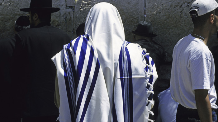 Gläubige Person mit einem weißen Gebetsmantel mit blauen Streifen.
