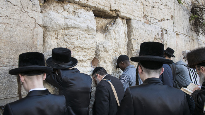Jüdische Männer mit Hüten oder Kippa stehen mit dem Rücken zum Betrachter an der Klagemauer in Jerusalem.