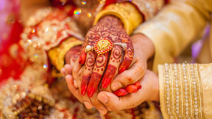 Die mit Henna verzierte und mit Ring geschmückte Hand einer Frau hält die Hand ihres zukünftigen Mannes.
