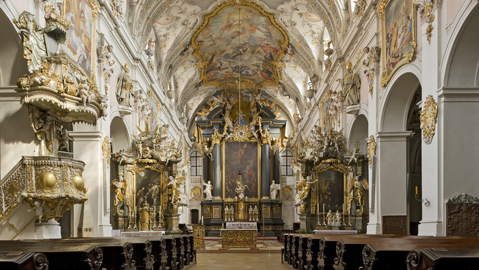 Blick in eine weiß und gold verzierte Kirche mit Deckenbemalung und reich geschmücktem Kirchenraum.