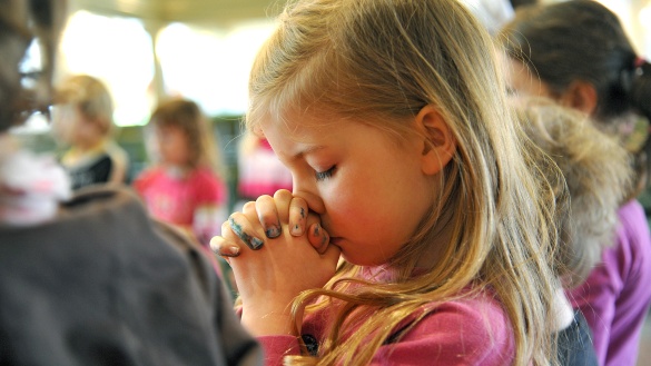 Ein Kind betet mit ausgestreckten Armen und geschlossenen Augen unter freiem Himmel. 