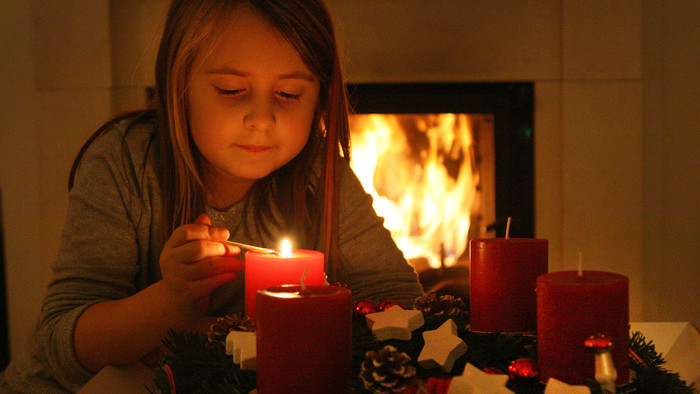 Mädchen zündet eine von vier roten Kerzen an einem Adventskranz an