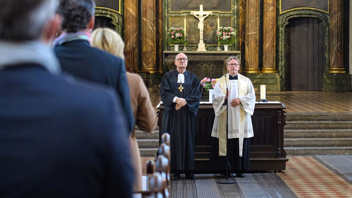 Evangelischer Pastor und Katholischer Pfarrer stehen vor dem Altar Richtung Gemeinde