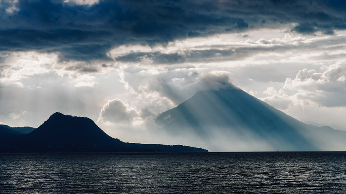 Wolken und Licht über einem sehr hohen Berg, der aus dem Wasser ragt