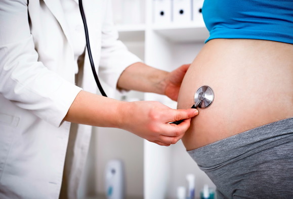 Ein Arzt hält sein Stethoskop auf den Bauch einer schwangeren Frau.