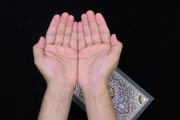 Betende Hände mit den Handflächen nach oben gerichtet über einem Koran.