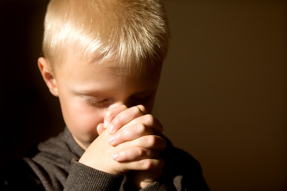 Ein blonder Junge betet mit gefalteten Händen.