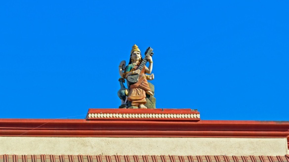 Statue der Hindu-Göttin Sarasvati mit dem Saiteninstrument Vina auf dem Dach eines Tempels