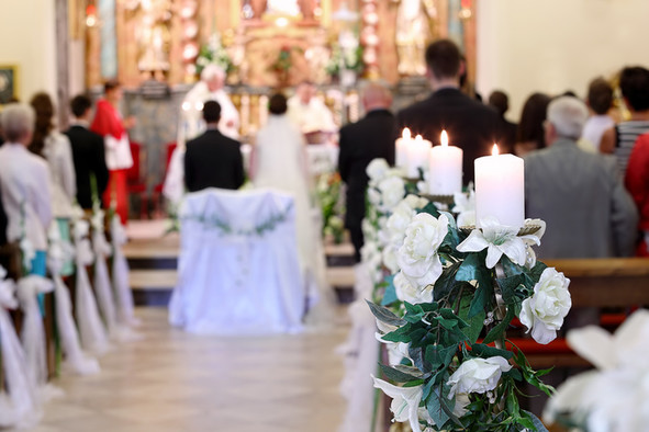 Ein Brautpaar steht vor dem Altar in einer mit weißen Blumen geschmückten, christlichen Kirche.