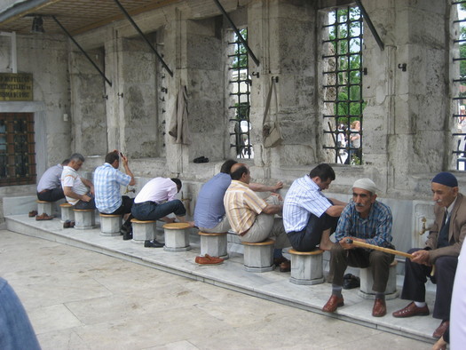 Männer sitzen auf Hockern vor Wasserhähnen einer Moschee und waschen sich.