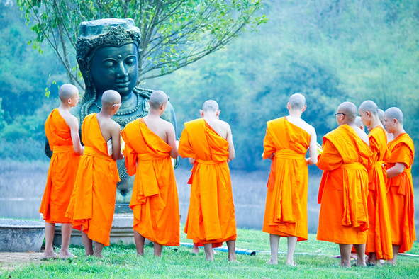 Zehn buddhistische Mönche in orangefarbenen Gewändern vor einer Buddhastatue.