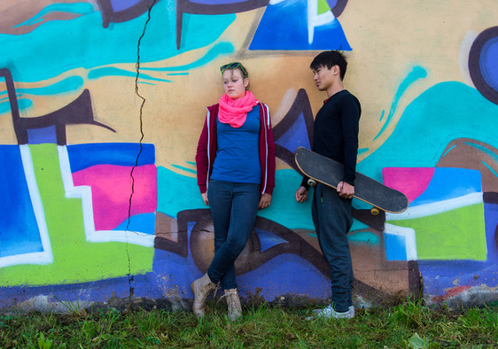 Mädchen und Junge mit Skateboard vor einer Wand mit bunten Graffiti.