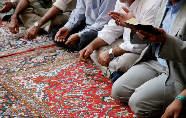Muslime knien auf einem roten Gebetsteppich mit bunten Mustern