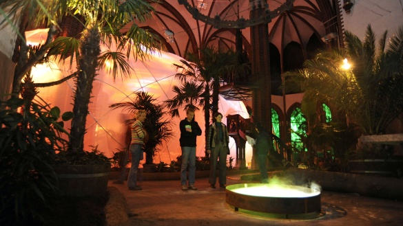 Menschen in einem als Paradies gestalteten Kirchenraum mit Palme und Brunnen.