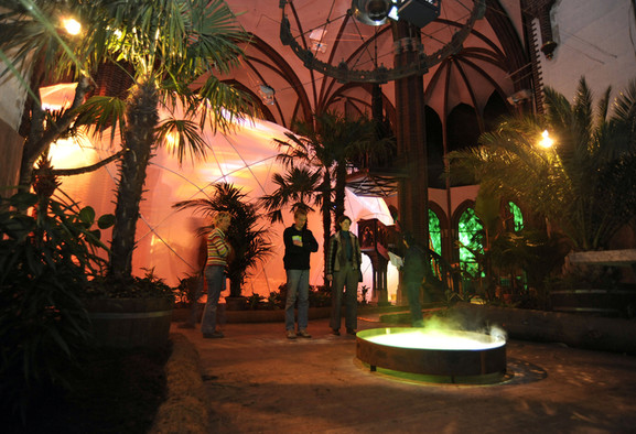 Menschen in einem als Paradies gestalteten Kirchenraum mit Palme und Brunnen.