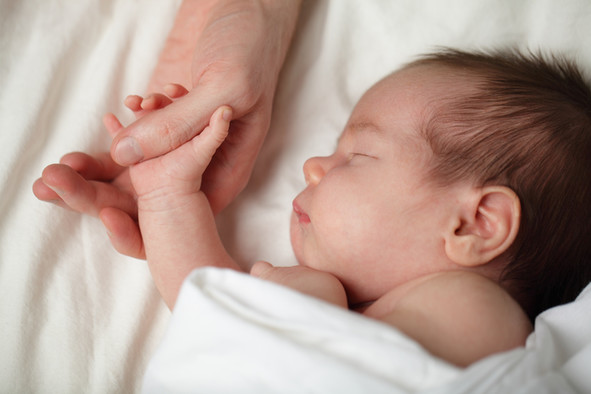Ein schlafendes Baby hält die Hand eines Erwachsenen.