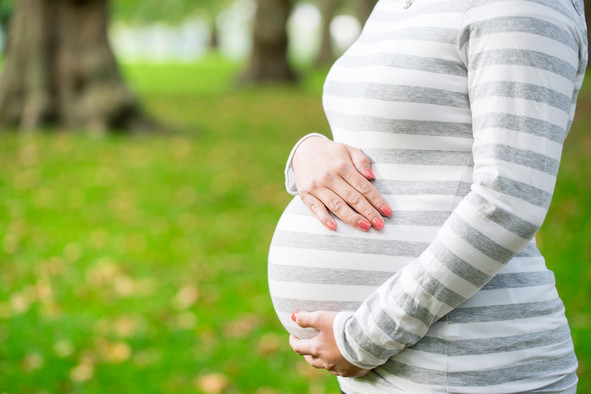 Eine schwangere Frau in einem grau-weiß geringelten T-Shirt umfasst ihren Bauch.