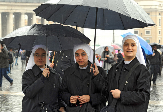 Zwei junge Ordensschwestern warten unter einem Regenschirm auf den Papst.