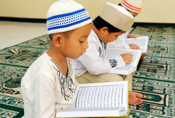 Drei Jungen lesen Suren im Koran.