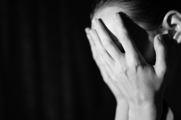 Bild in schwarz-weiß von einer verzweifelten jungen Person, die sich beide Hände vor ihr Gesicht hält.
