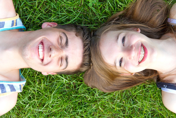 Junger Mann und junge Frau liegen Kopf an Kopf auf einer Wiese.