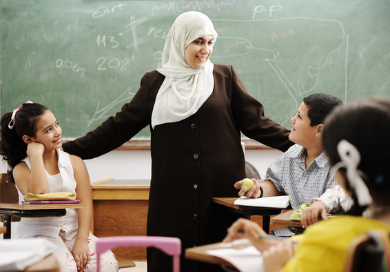 Eine muslimische Lehrerin begrüßt Kinder in der Klasse.