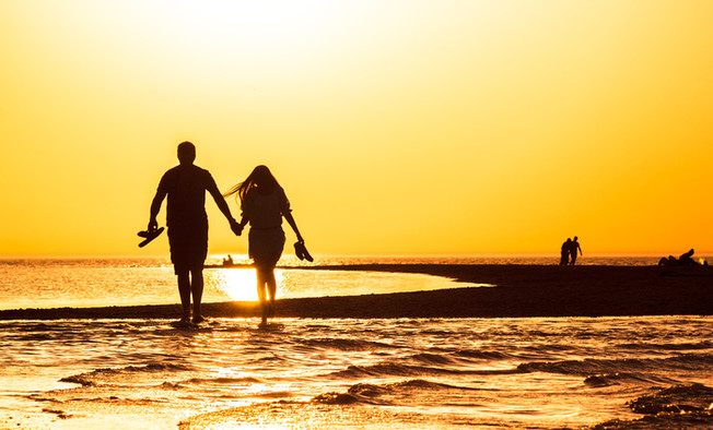 Silhouette eines Paares, das sich an den Händen hält und im Sonnenuntergang am Strand entlang läuft.