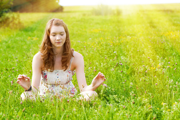 Eine junge Frau sitzt auf einer Wiese und meditiert.
