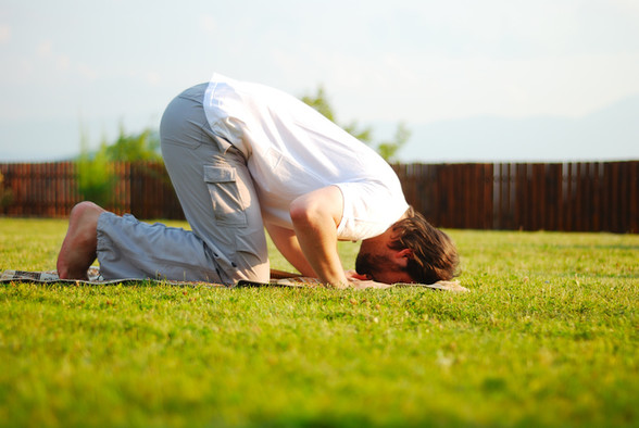 Ein Muslim berührt beim Beten auf einer Wiese mit der Stirn das Gras