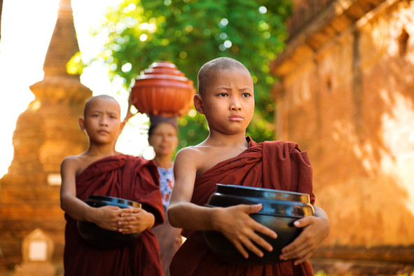 Zwei junge buddhistische Mönche aus Myanmar in braunem Gewand tragen Schüsseln vor dem Körper.
