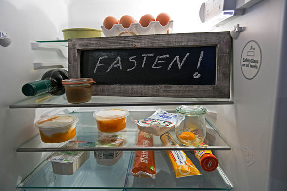 Ein geöffneter Kühlschrank mit Lebensmitteln und einem Schild "Fasten!".