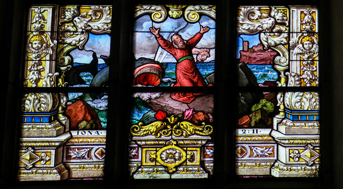 Kirchenfenster aus buntem Glas mit der Szene von Jona im Boot, kurz bevor er vom Walfisch verschluckt wird.