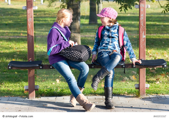 Zwei Mädchen an einer Bushaltestelle unterhalten sich.
