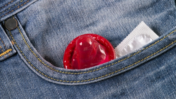 Ein rotes und ein weiß verpacktes Kondom stecken in der Tasche einer Jeans.