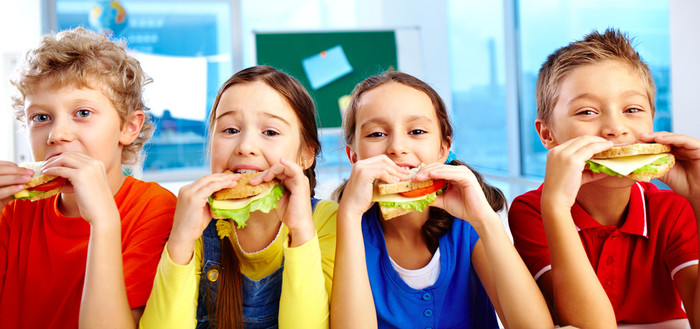 Zwei Mädchen und zwei Jungen beißen mit Appetit in ein Sandwich.