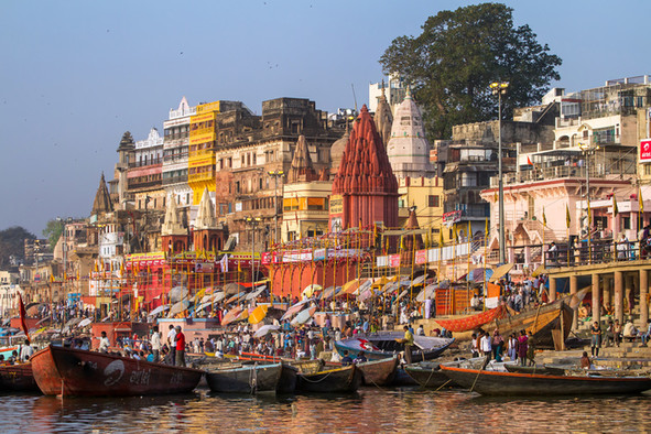 Blick vom Fluß Ganges auf den Hafen der indischen Stadt Benares mit vielen bunten Schiffen und Häusern.
