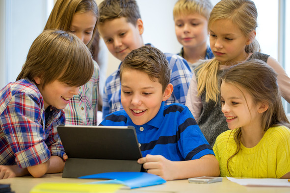 Zwei Mädchen und drei Jungs schauen sich im Unterricht etwas auf einem Tablet an.