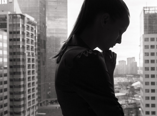 Schwarz-weiß Silhouette einer jungen Frau an einem Fenster, im Hintergrund eine Großstadt.