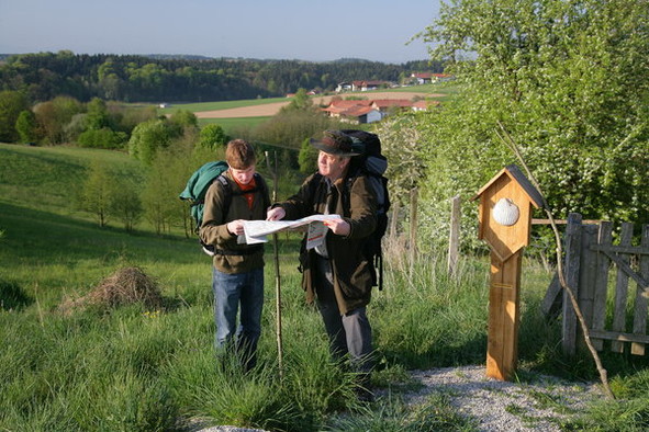 Zwei Pilger mit Rucksack, unterwegs auf dem Jakobsweg bei Altötting in Oberbayern, schauen auf eine Karte.