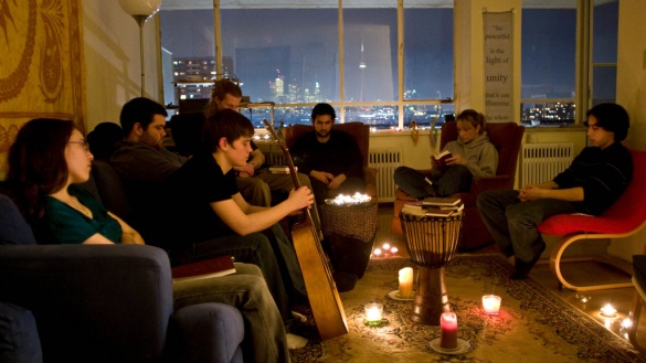 Menschen sitzen bei einer Andacht in einem Zimmer im Kreis. In der Mitte stehen brennende Kerzen.