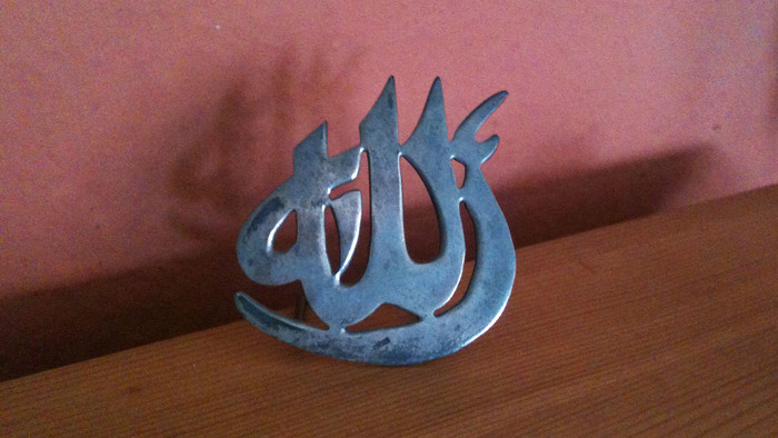 Das arabische Schriftzeichen für Allah aus Metall an einem Holzbrett.