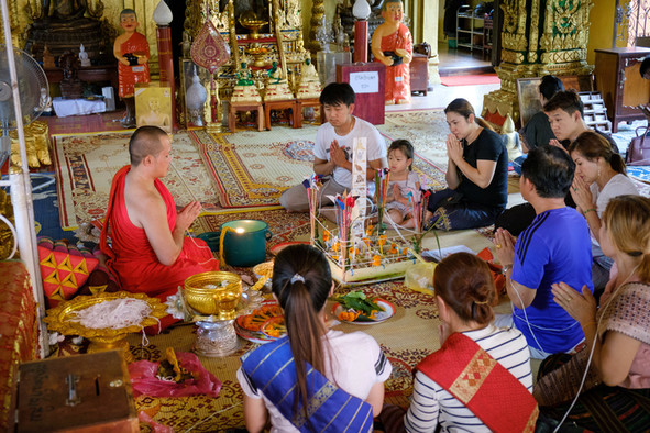 Ein Mönch und weitere Menschen sitzen auf dem Boden eines Tempels mit betenden Händen.