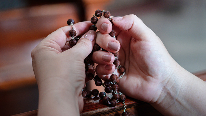 Zwei Hände mit lackierten Fingernägeln halten einen Rosenkranz und zählen die Perlen mit den Fingern ab.